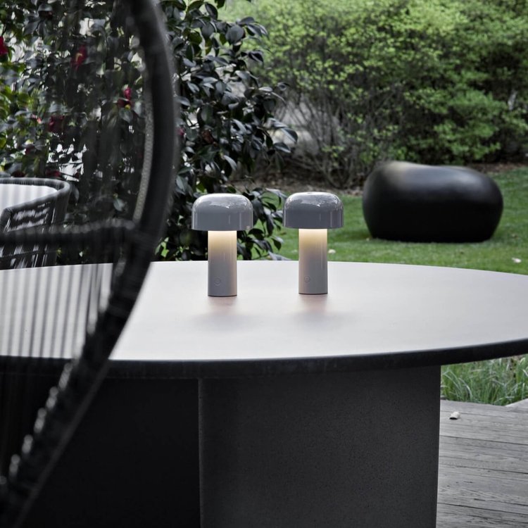 Two small lit lamps on a round outdoor table with a garden behind 23