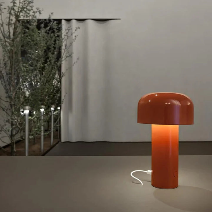 Orange-red lamp glowing on a table with a white charging cable plugged into its base 25