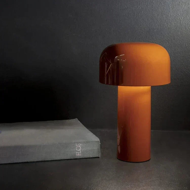 Burnt orange mushroom lamp glowing on a dark surface next to a gray book 8