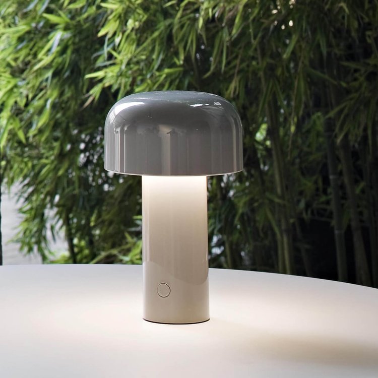 Gray lamp lit on a round white table with green bamboo behind it 9