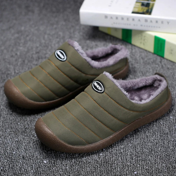 Pair of olive green quilted slippers with gray fleece lining on a gray carpet beside books 2