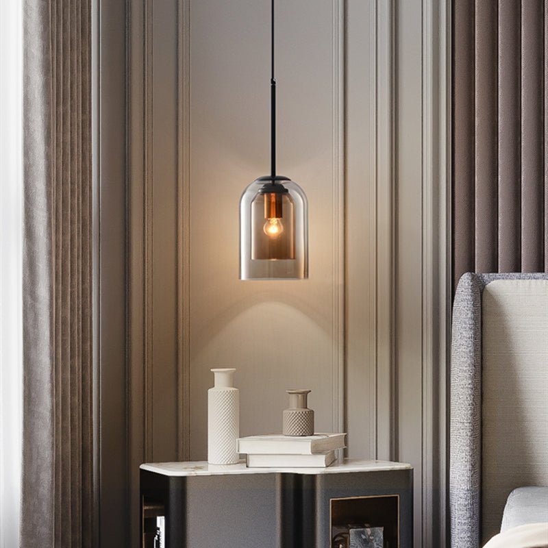 Smoky glass pendant lit above a marble-topped nightstand with vases and books beside a bed 2