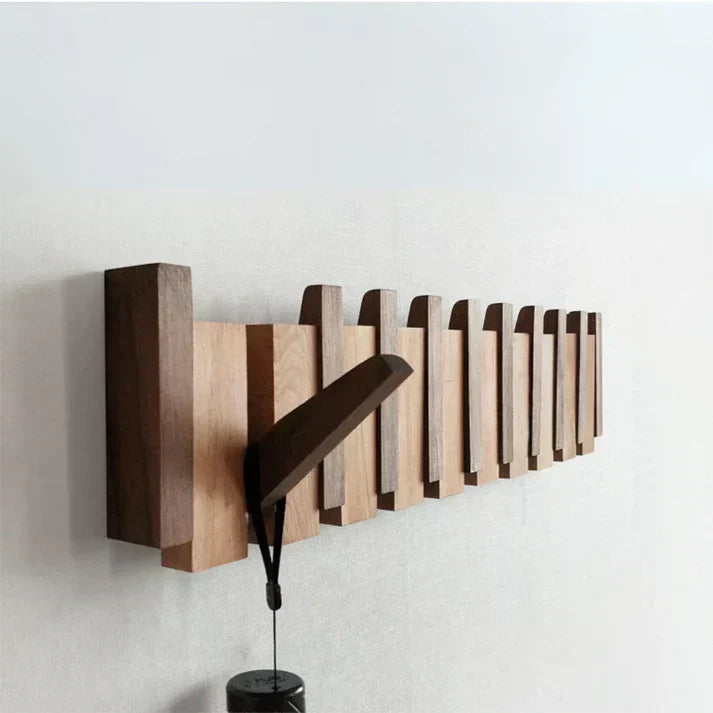 Side-angle view of the wall-mounted wooden rack with one hook folded out holding a dark strap 1